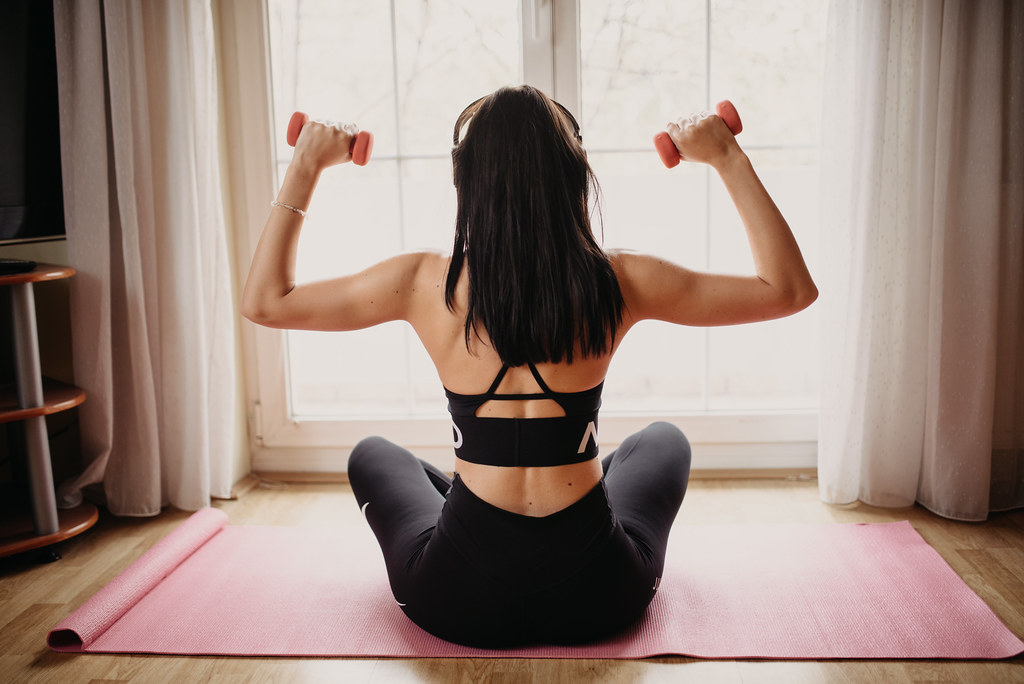 Mujer entrenando con mancuernas en casa sobre una esterilla